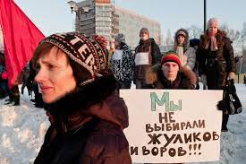یک معترض با کلاه در مقابل تابلویی به زبان روسی ایستاده است که ترجمه آن به "ما به کلاهبرداران و دزدها رای ندادیم!"